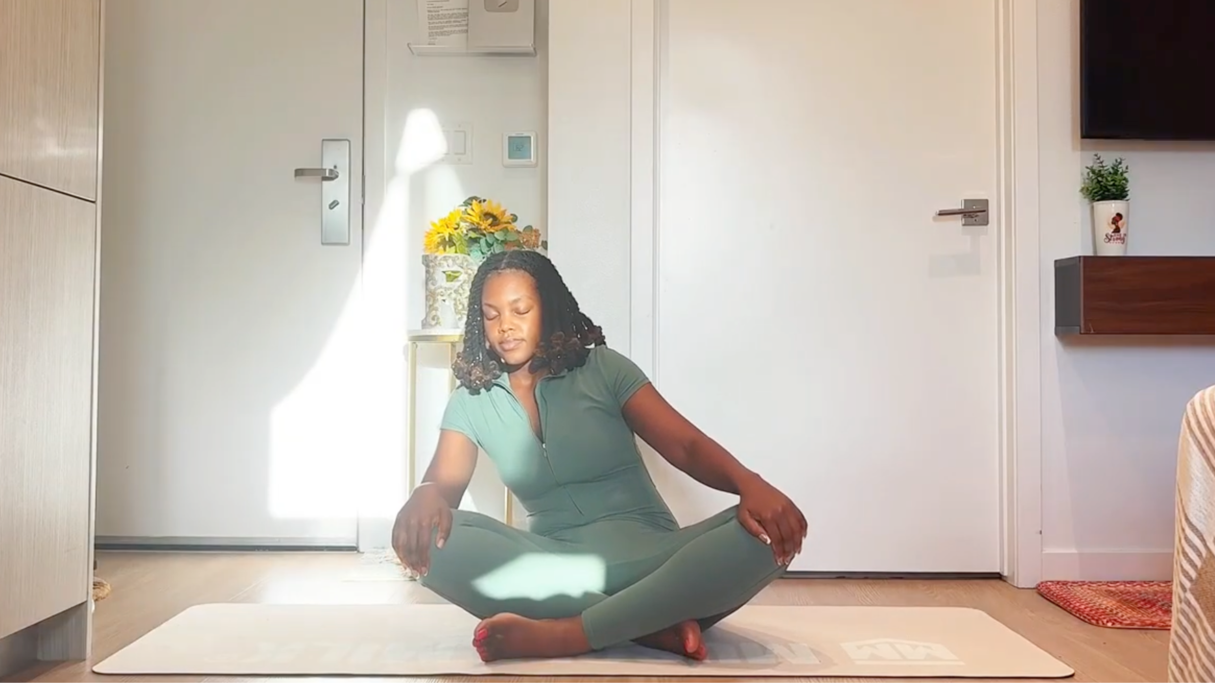 Ramoni Overton seated on a yoga mat, leaning forward and circling torso to warm up the spine and relieve back stiffness.